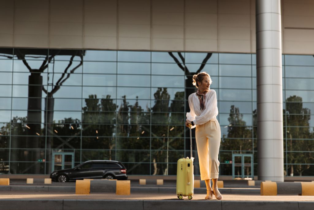 Charming blonde woman in white blouse, beige pants and eyeglasses moves near airport. Pretty girl i